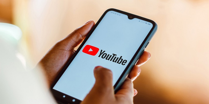 A person holds a smartphone displaying the YouTube logo on its screen, highlighting the importance of captioning for accessibility.