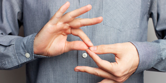 A person wearing a gray button-up shirt uses both hands to perform a gesture, possibly as a BSL interpreter, against a neutral background.