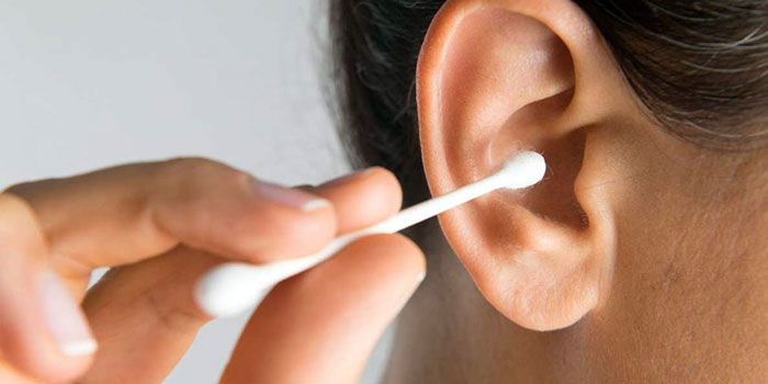 A person holding cotton buds near their ear, preparing to clean it.