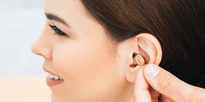 A person is inserting a small beige hearing aid into their right ear, with a close-up focus on the ear and device, offering a visual hearing aid guide for new users.