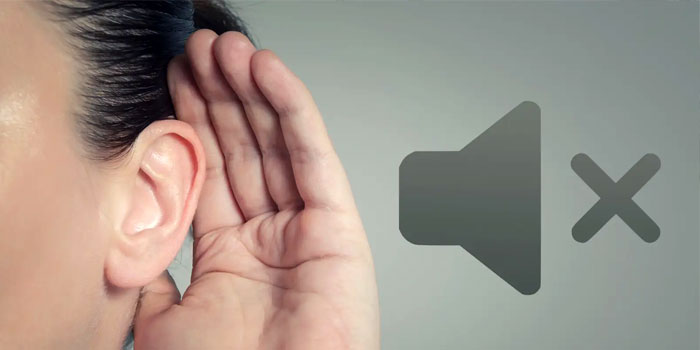 A person holds a hand behind their ear as if trying to hear, with a muted speaker icon next to them, illustrating hearing loss.