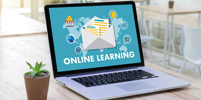 A laptop on a wooden desk displays an "Online Learning" graphic with icons for communication, shopping, and education; a small potted plant is beside the laptop, highlighting the importance of captions in online learning environments.