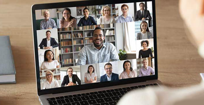 A person participates in a video conference on a laptop with fifteen others, all visible in a grid of small windows, while live captioning ensures everyone can follow the conversation.