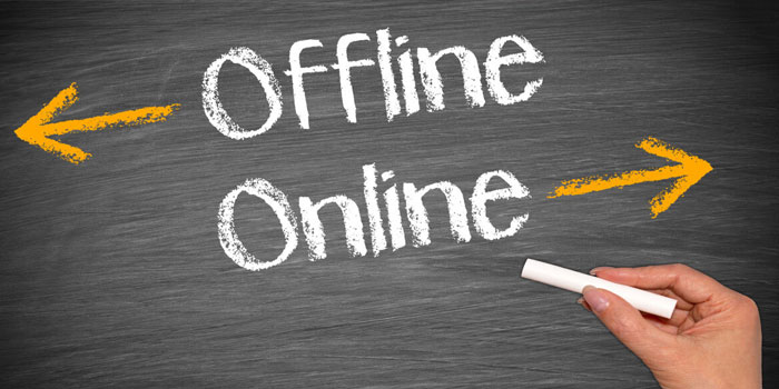 A hand holds chalk near the words "Offline" and "Online" on a chalkboard, with arrows pointing left for "Offline" and right for "Online," illustrating the shift to digital tools like live captioning.