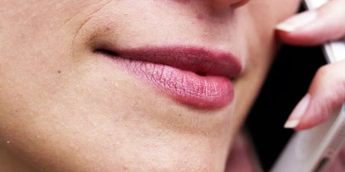 Close-up of a person's mouth and chin as they hold a phone to their ear, appearing to use an oral translator during a conversation.