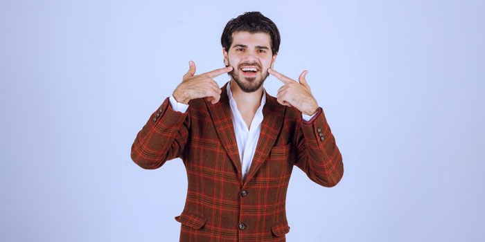 A man in a red plaid suit points to his smiling mouth with both index fingers, symbolizing the clarity and connection provided by expert Oral Translators, against a plain light background.