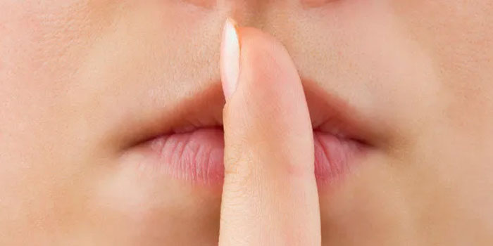 A close-up of a person's lips with an index finger held vertically in front, suggesting silence—much like an oral translator signaling the need for quiet before interpreting.