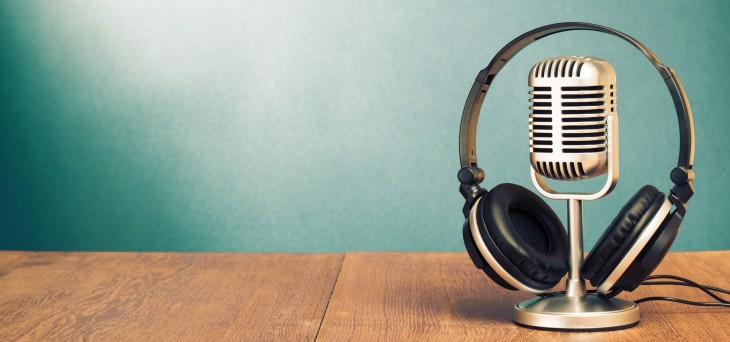 A vintage-style microphone with a pair of black headphones rests on a wooden table against a blue-green gradient background—perfect for creators looking to transcribe your podcast in style.