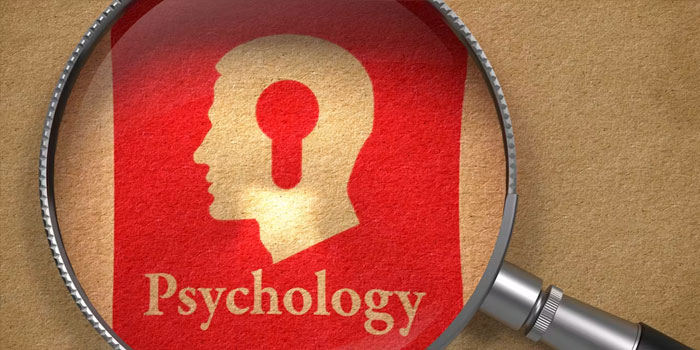 A magnifying glass focuses on a red paper with a human head silhouette featuring a keyhole, above the word "Psychology," perfect for business captions exploring the connection between mindset and professional growth.