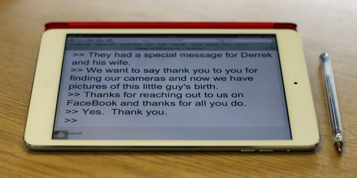 A tablet displaying a message about finding cameras and sharing photos sits on a wooden surface next to a pen, highlighting the use of remote captioning services for enhanced accessibility.