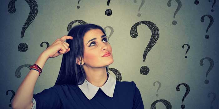 A deaf woman scratches her head and looks up, standing in front of a background filled with large question marks.