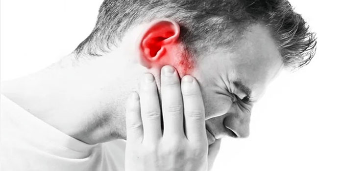 A man holds his ear in pain, with the ear area highlighted in red to indicate discomfort or infection, possibly due to tinnitus.