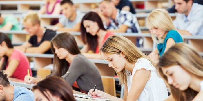 Students, including those with hearing loss, sit in a lecture hall, writing in notebooks and staying focused on their work during a class or exam.